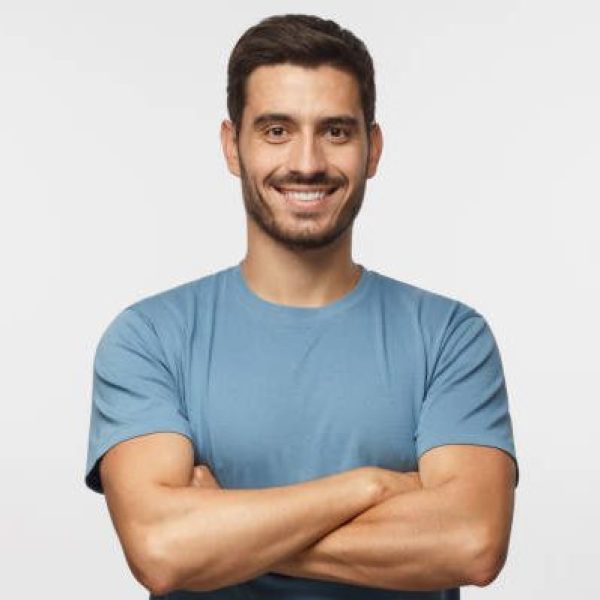 Portrait of smiling handsome man in blue t-shirt standing with crossed arms isolated on grey background